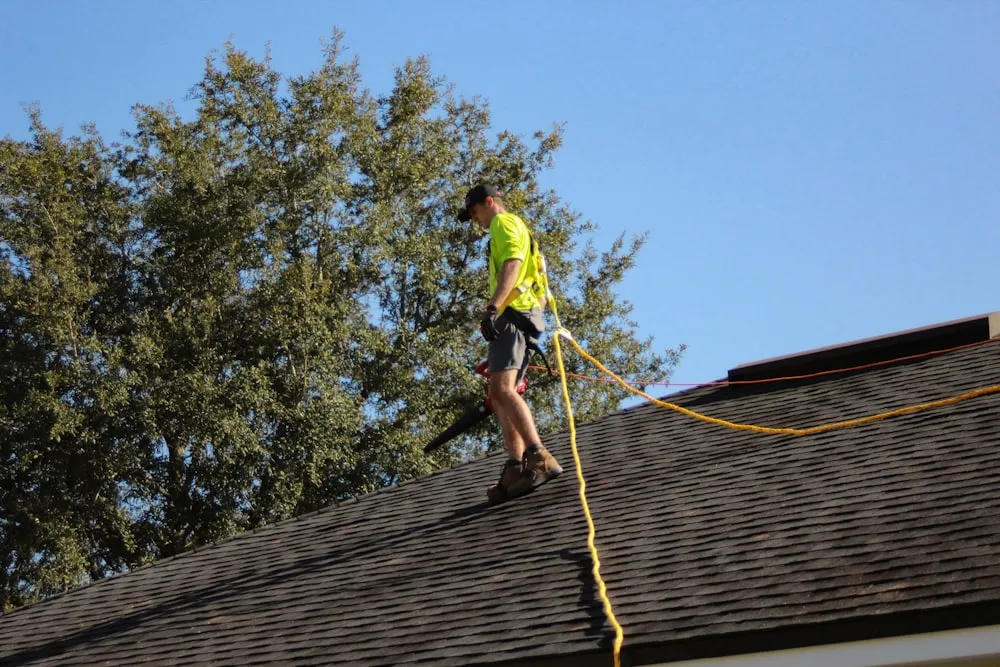 Roofer safety-tied installing new shingles